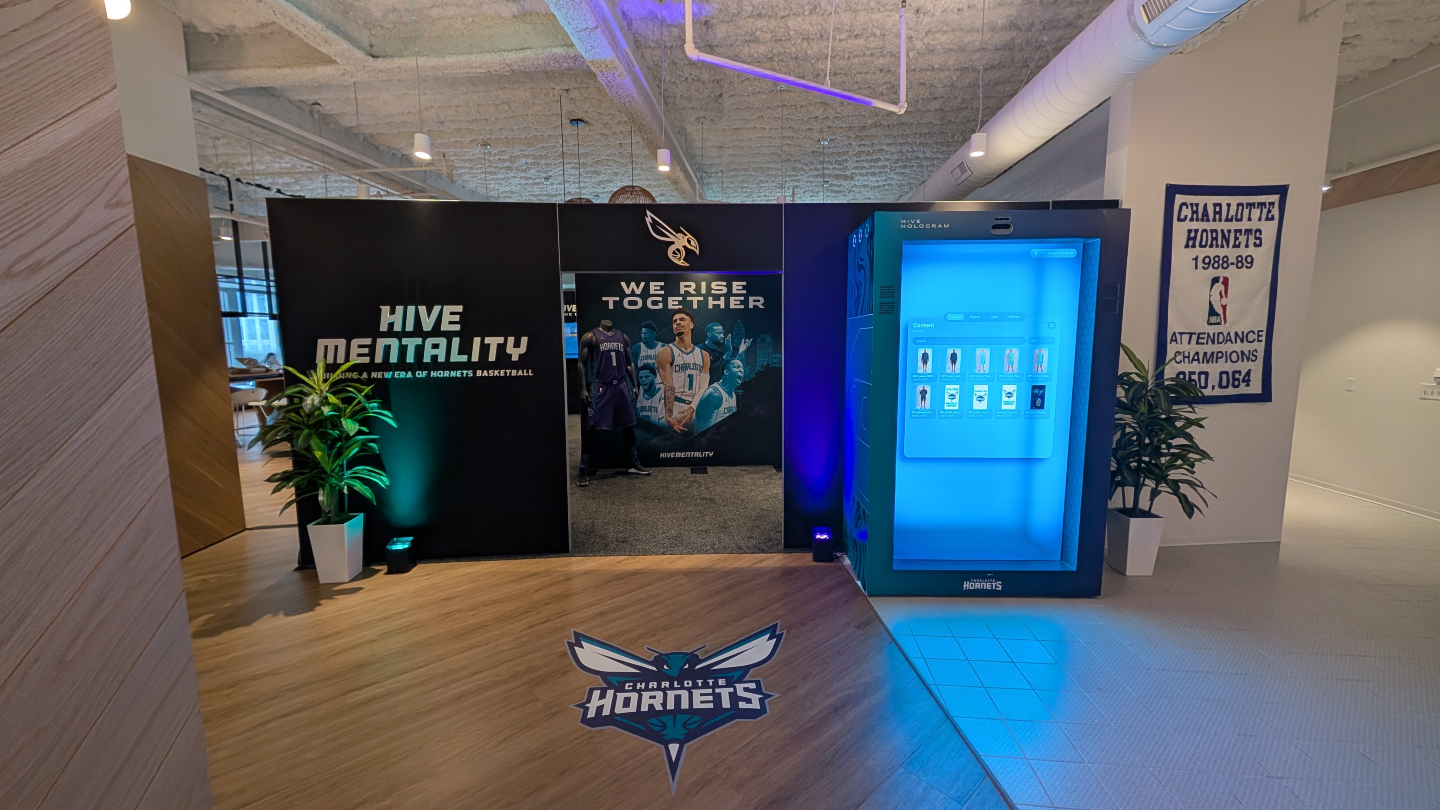 Charlotte Hornets branded area with "Hive Mentality" wall, player mural, glowing blue hologram booth and team logo on the floor