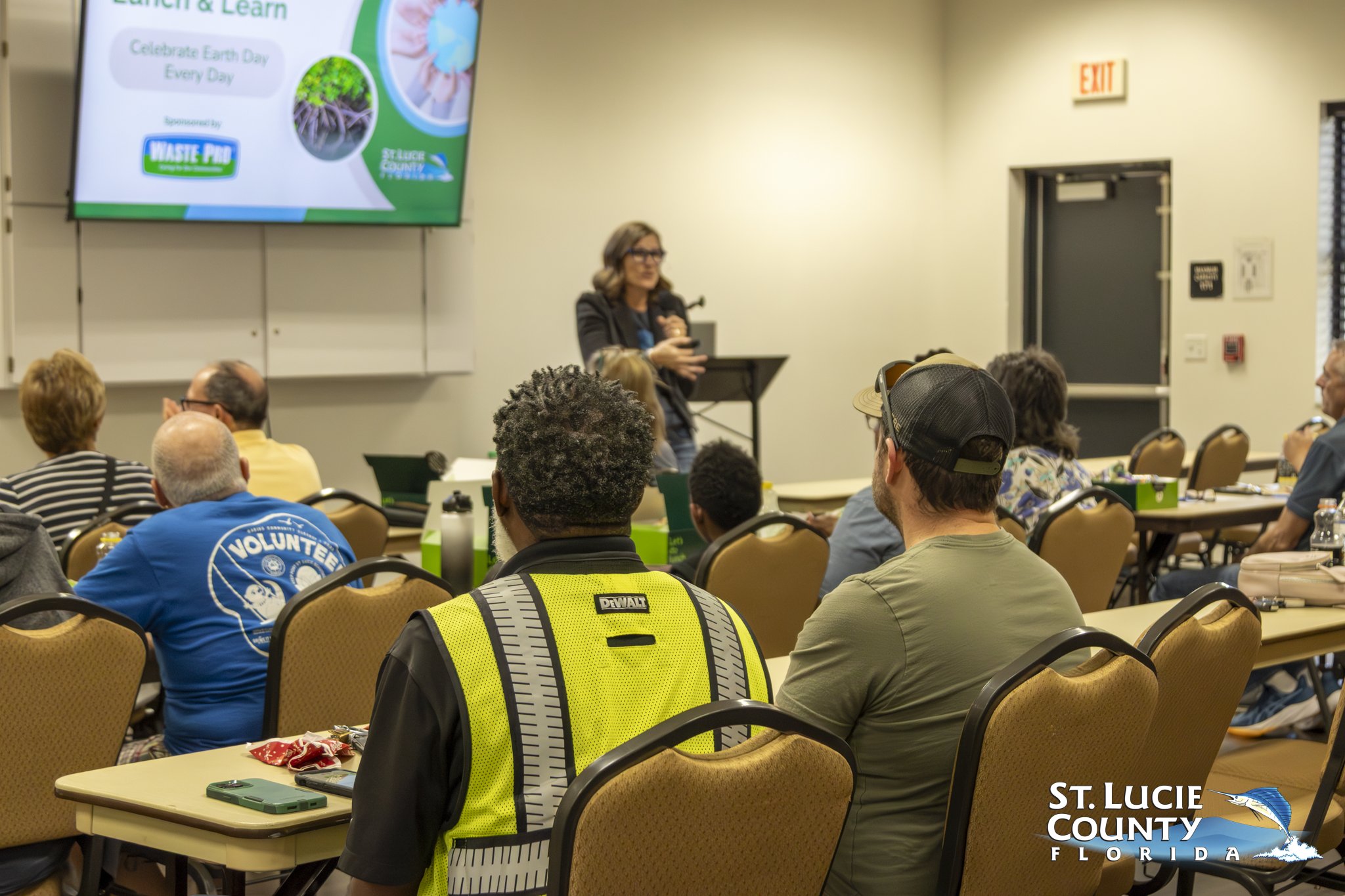 Audience attentively listens to a speaker presenting Earth Day and waste reduction tips in a community room.