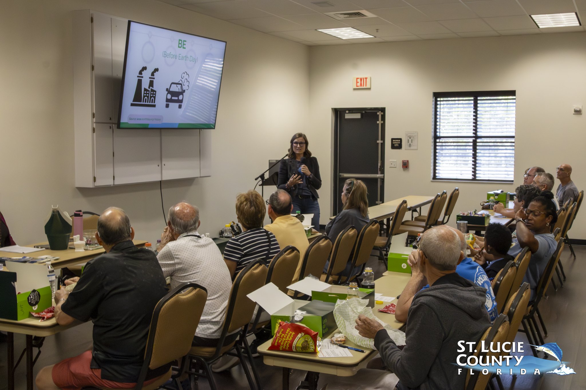 Woman presenting environmental tips on reducing pollution to an attentive classroom audience in St. Lucie County, Florida.