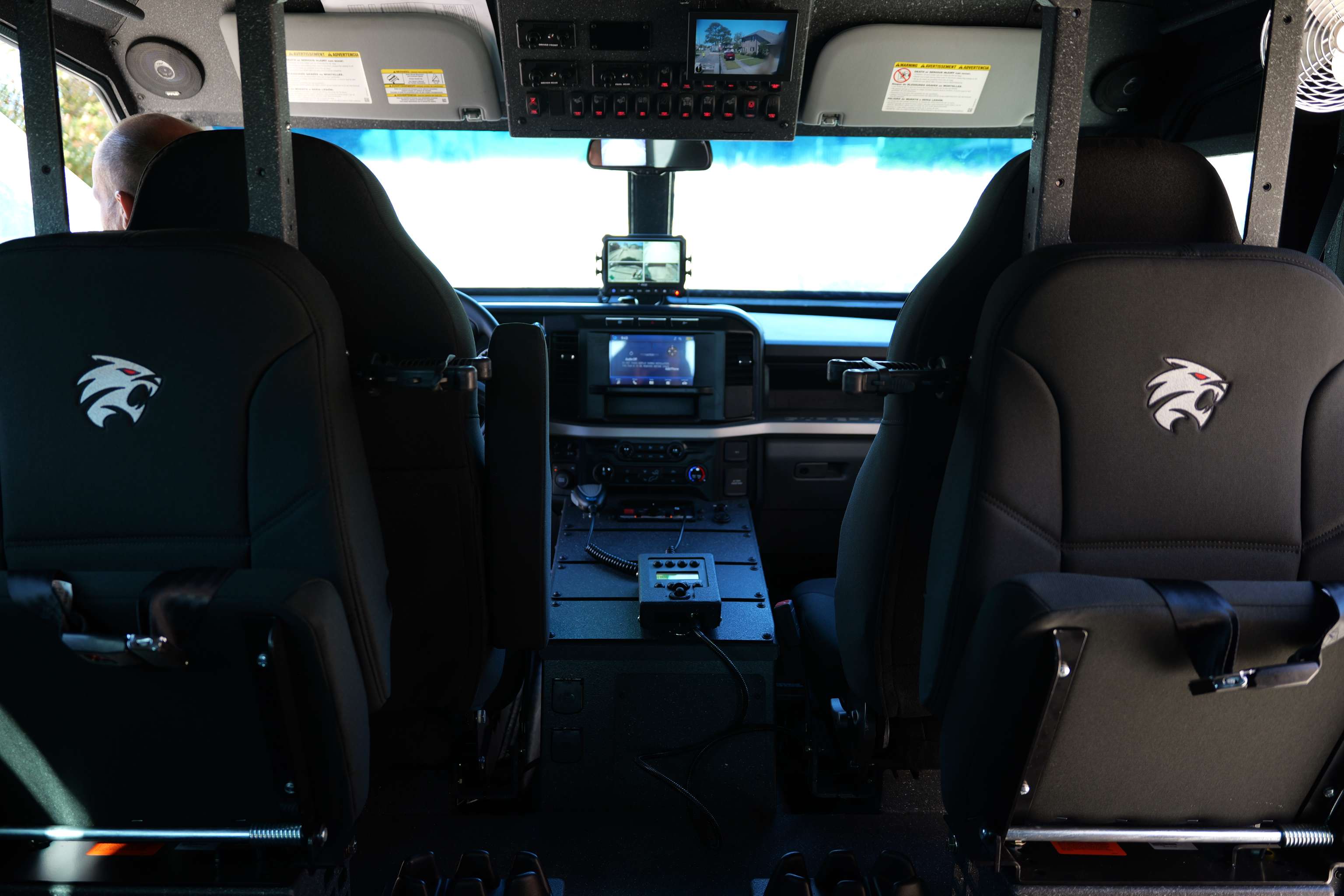 Interior view of a vehicle cabin showing two black front seats with eagle logos and a dashboard equipped with multiple screens and controls.