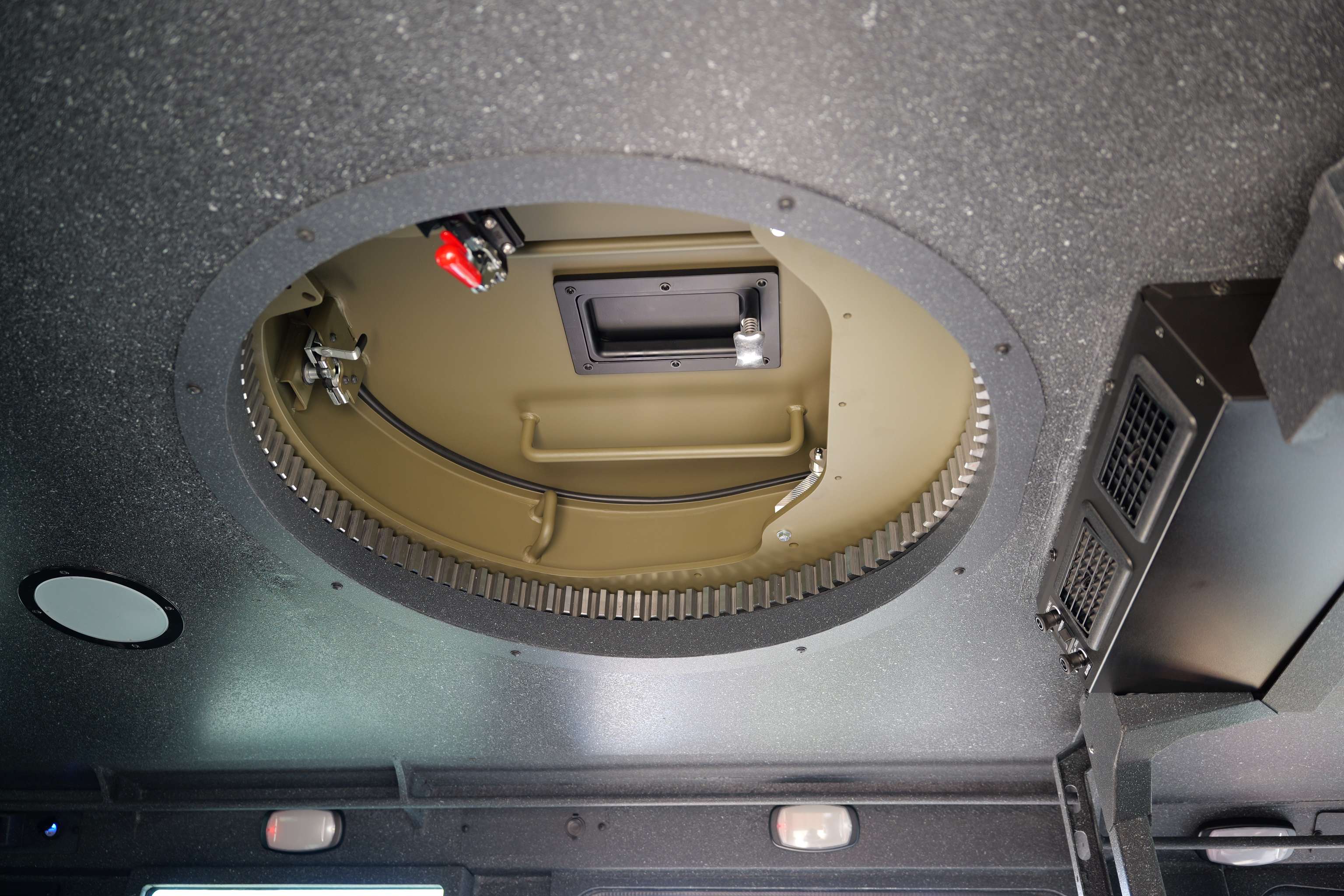 Interior view of a circular hatch on a vehicle ceiling with mechanical components and wiring visible inside.