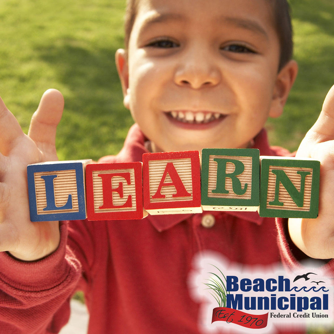 Young boy smiling and holding colorful wooden blocks spelling LEARN outdoors on a sunny day.
