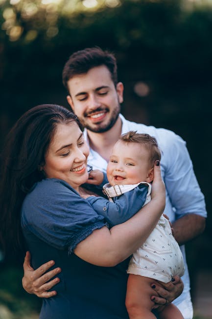 A joyful family portrait outdoors featuring parents holding their smiling baby together.