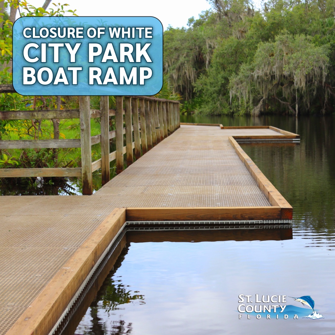 Empty wooden boat ramp extending into calm water surrounded by lush green trees at White City Park with text alerting residents of it's closure.