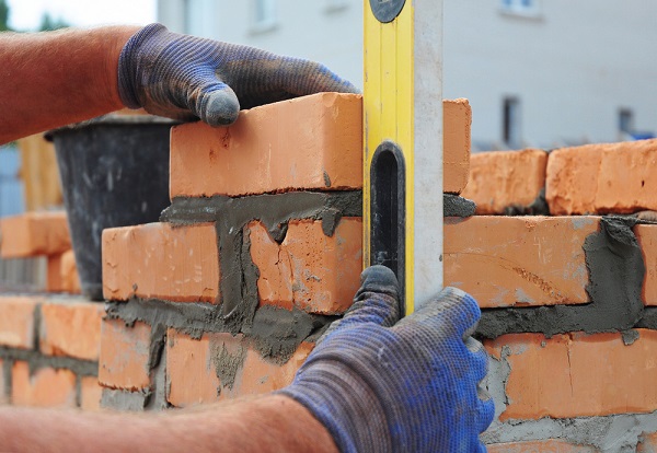 close-up of gloved hands using a spirit level against a partially built brick wall