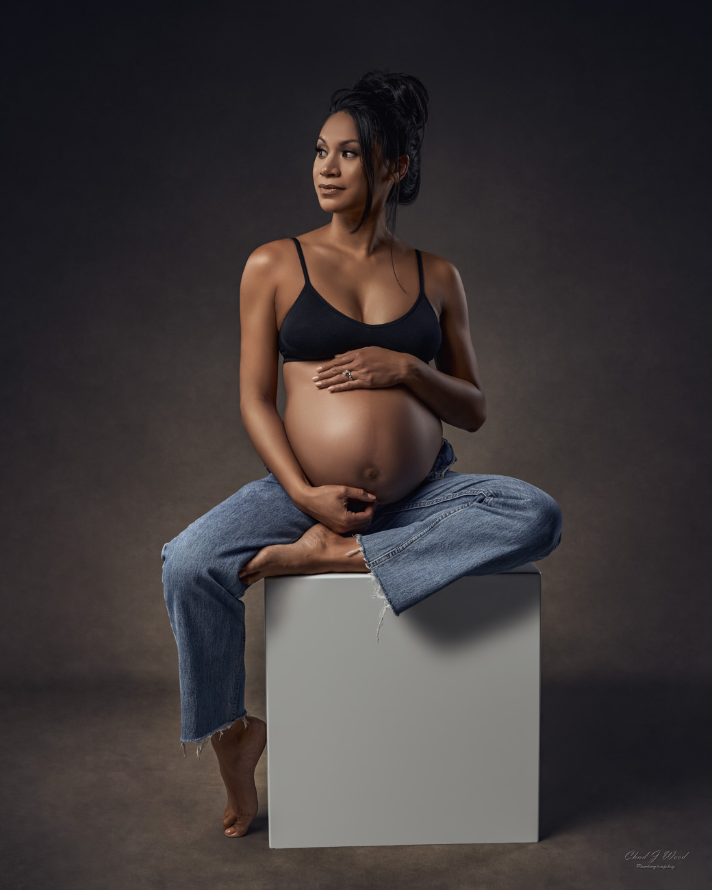 Phoenix Maternity Photography: Pregnant woman in blue jeans sitting on a box cradling her belly.
