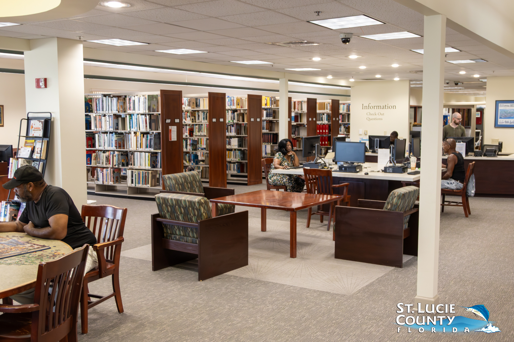 Spacious library interior with bookshelves, seating areas, and patrons reading or using computers.