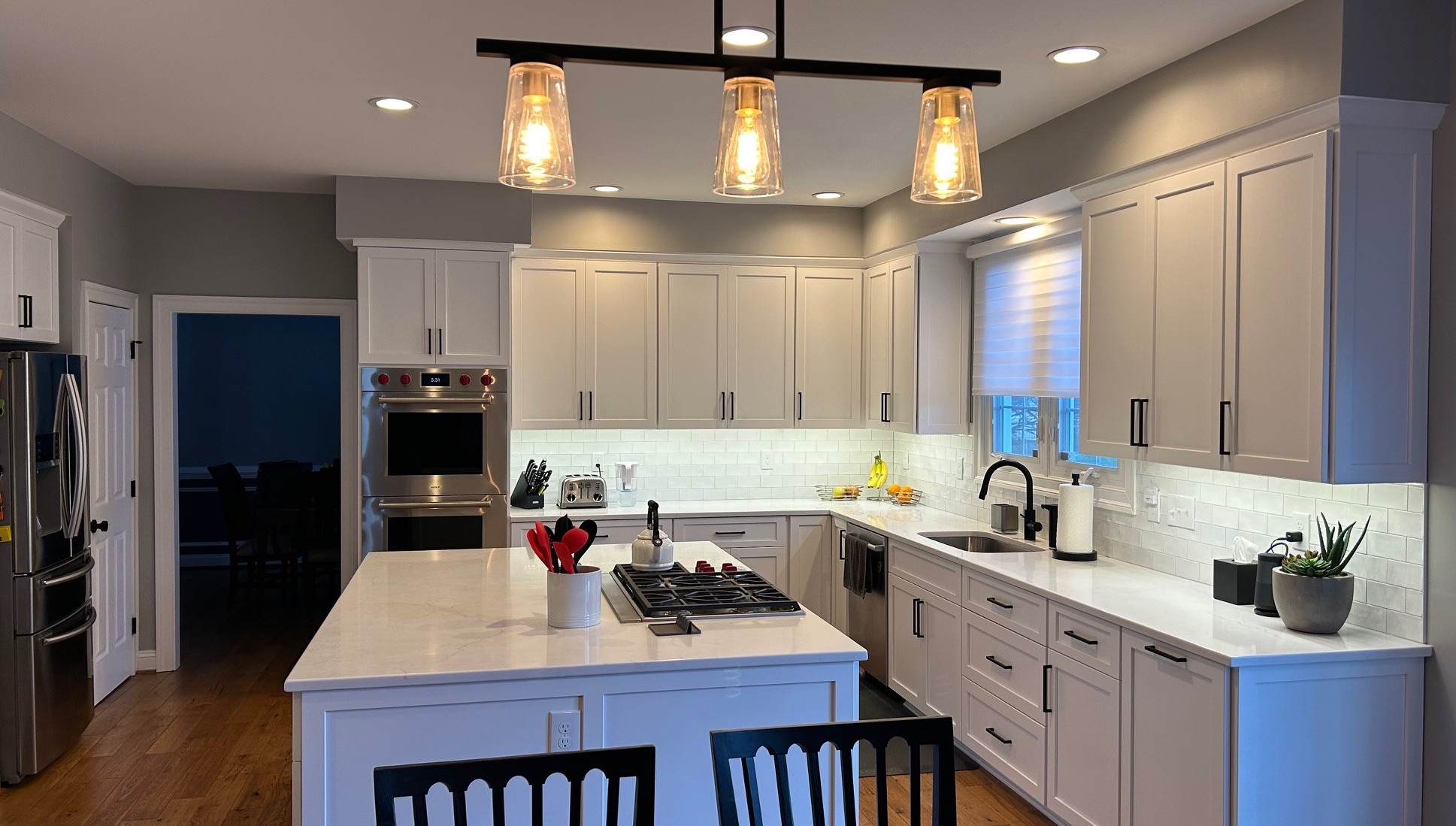 We recently completed this stunning kitchen remodel in Olney, MD, blending the best of contemporary and traditional design elements for a truly functional and beautiful space.
Clean Lines and Clever Details
This transitional kitchen features white Shaker-style cabinetry that provides a timeless foundation. We paired the classic cabinets with sleek, matte black hardware for a modern, industrial touch. To create a bright and open feel, we installed white subway tile backsplashes with under-cabinet LED lighting that highlights the stunning polished quartz countertops.
A Focus on Function
The expansive center island is designed for maximum utility. It features a flush-mounted gas cooktop and plenty of extra storage, making it the perfect hub for both meal prep and entertaining. For added convenience, we integrated a dedicated beverage station with a wine cooler and ample counter space for a coffee bar.
Ready to transform your kitchen? Contact Talon Construction Inc. for a consultation.