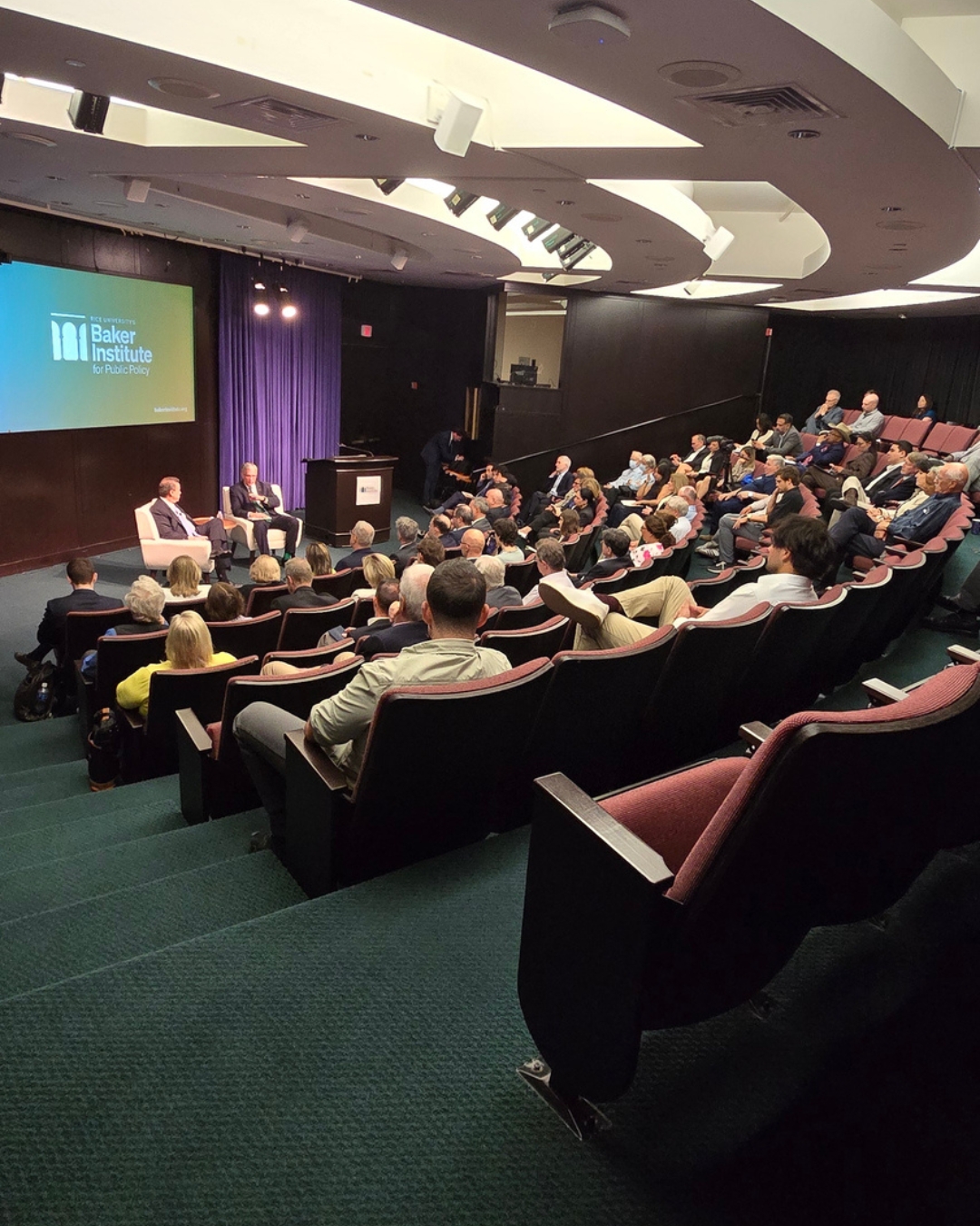 H.E. Stavros Papastavrou (left) and Ken Medlock (right) on stage in an auditorium.