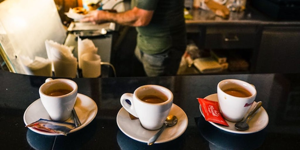 A barista in a café preparing espresso drinks on a countertop with three coffee cups in focus.