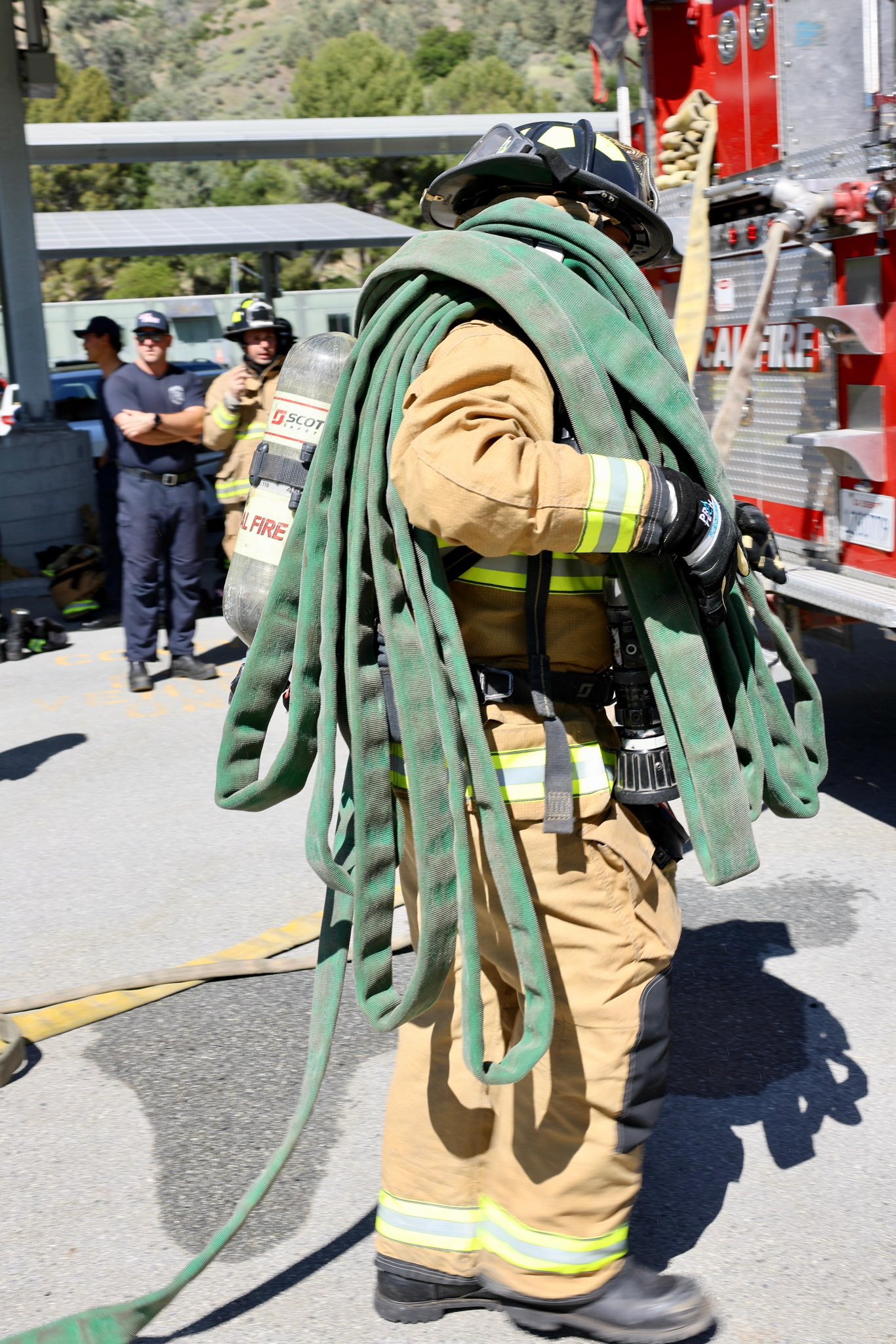 (CAL FIRE) firefighter wearing structural turnout gear carrying hose on his shoulder