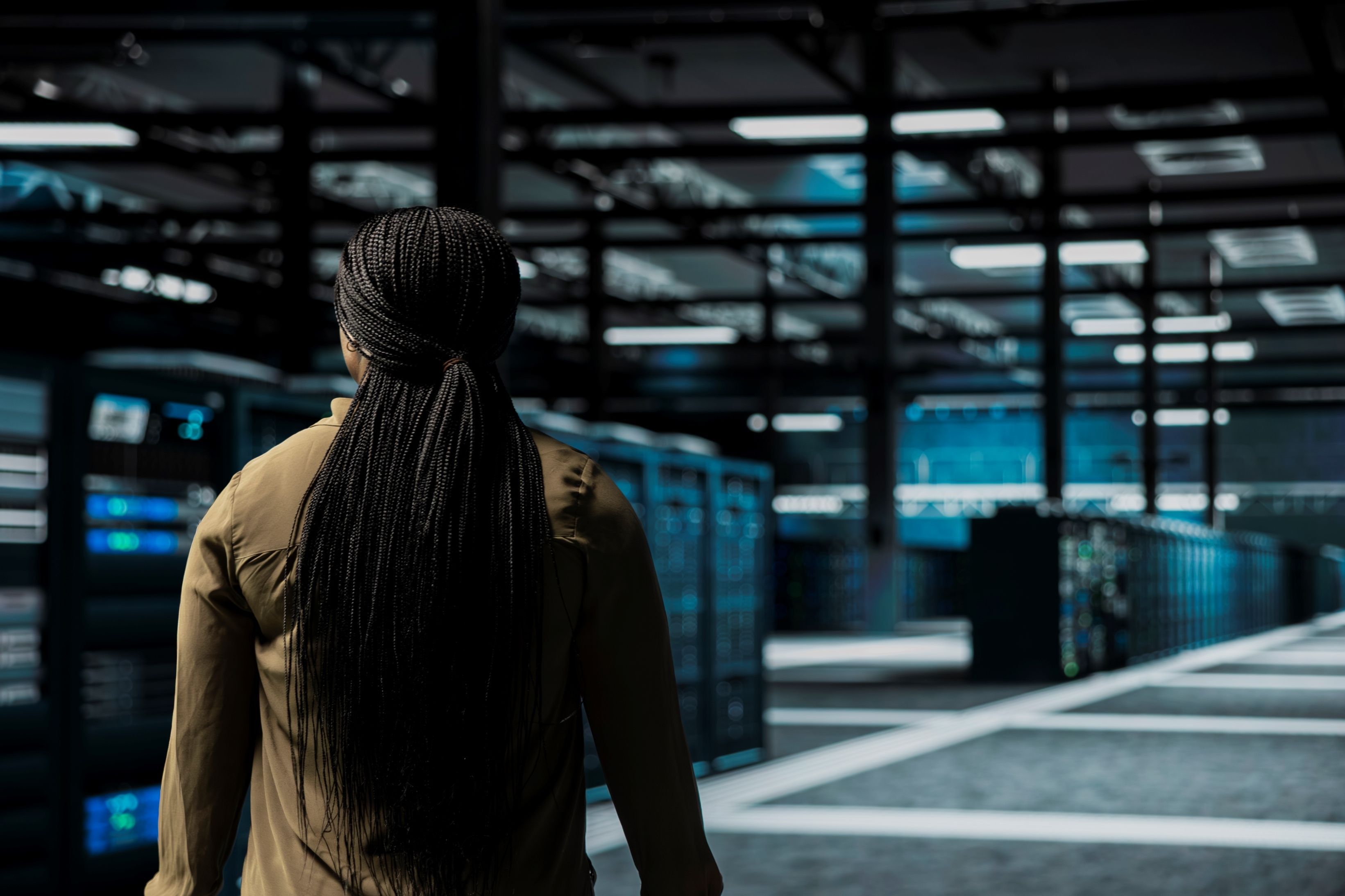A software developer walks among server room rows lined with storage infrastructure rigs in a data centre. Photo: DC Studio on Freepik.