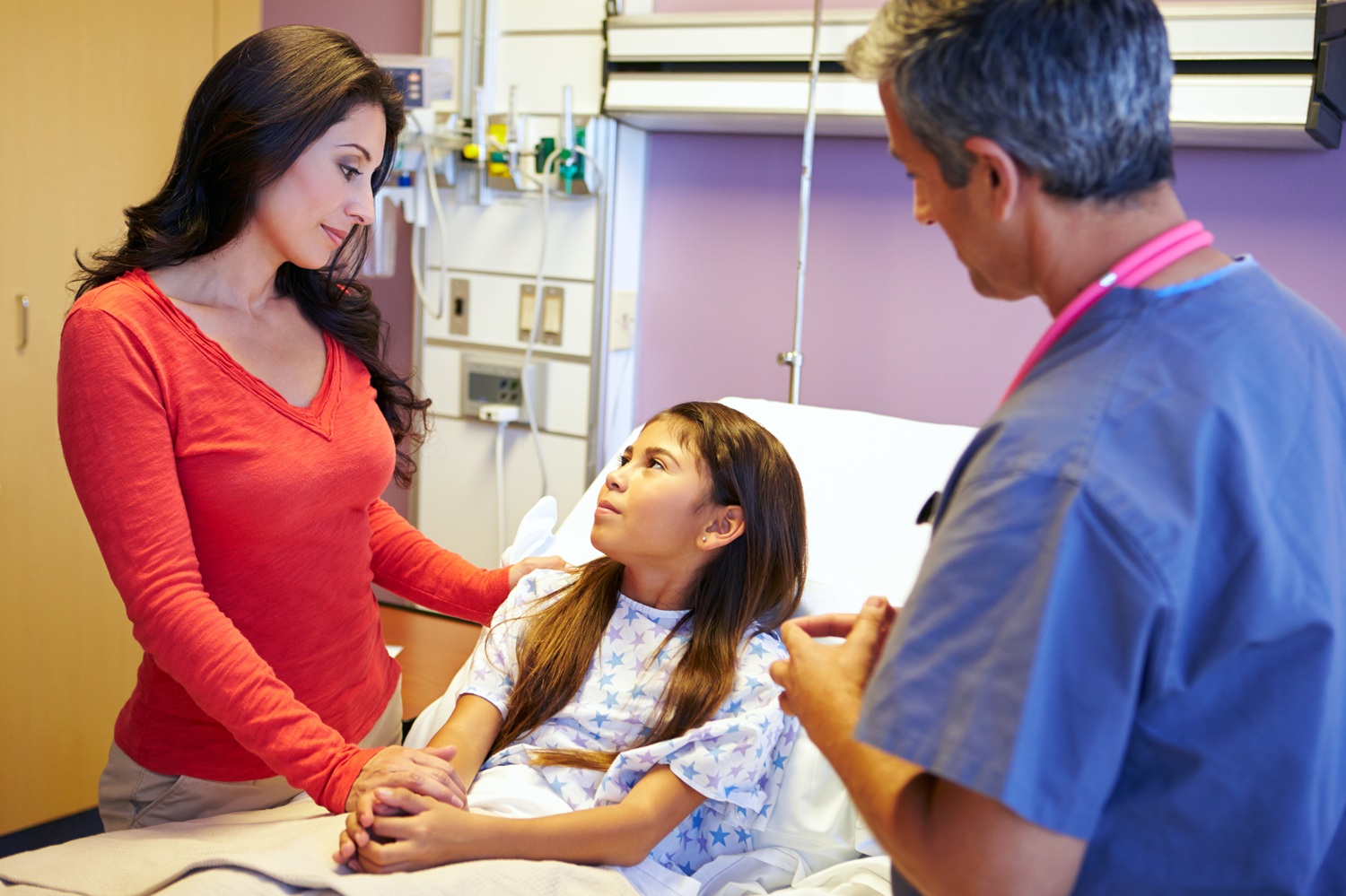An adult is holding hands with a child who is lying in a hospital bed while a doctor discusses her care.