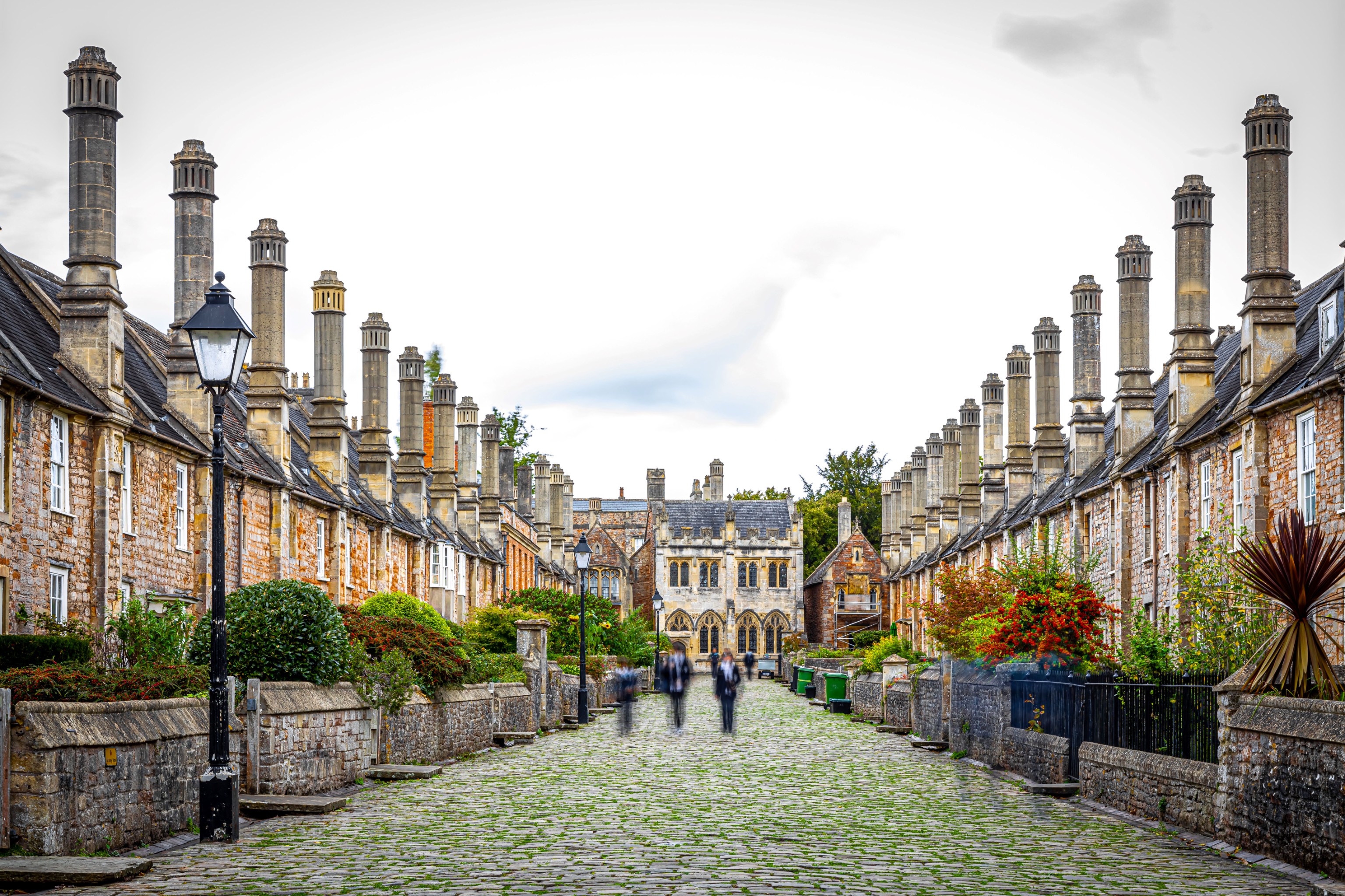 Cobblestone street lined with historic brick houses featuring tall chimneys under a cloudy sky.