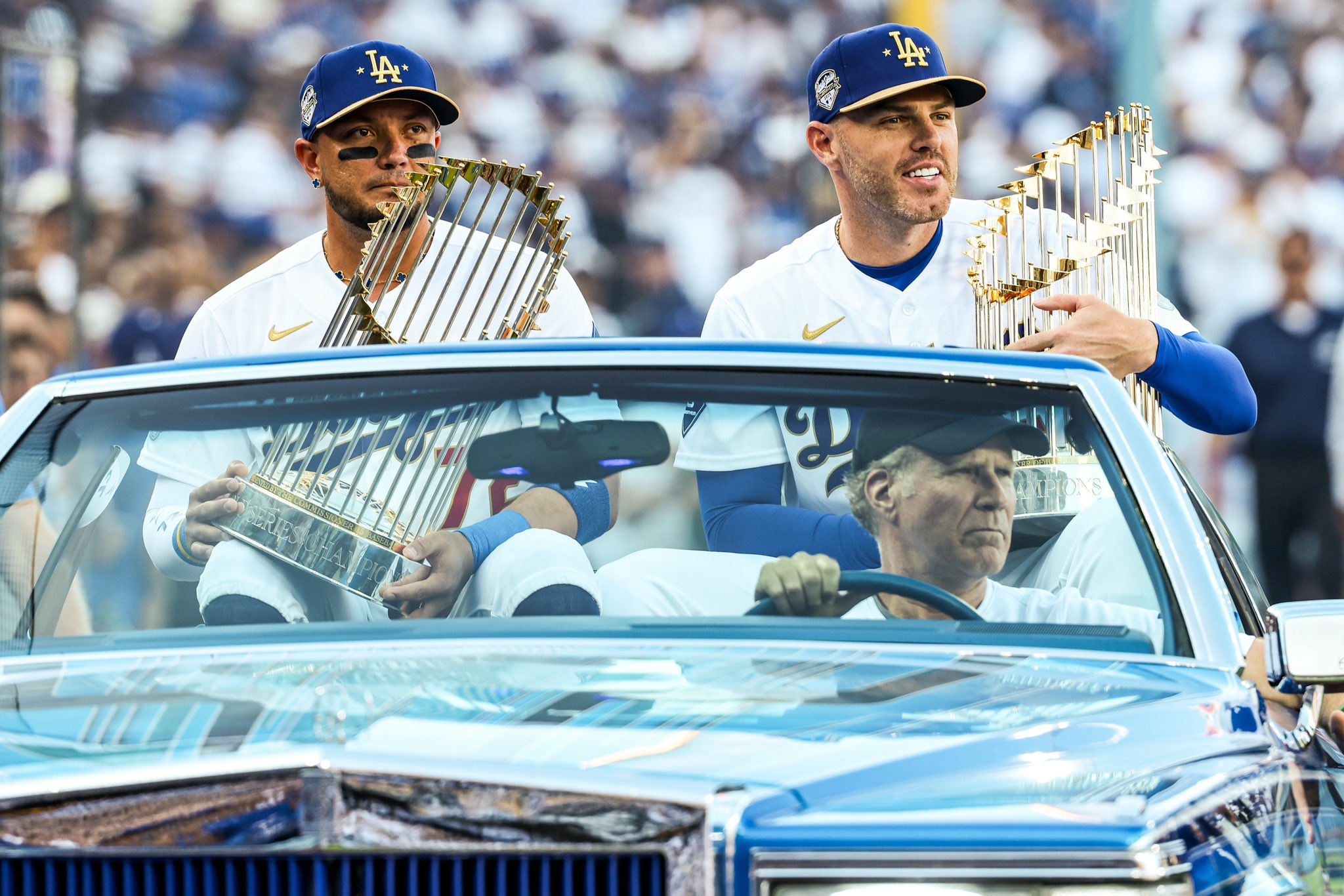 Miguel Rojas y Freddie Freeman sostienen los trofeos de campeones de la Serie Mundial 2024 y 2025 mientras Will Ferrell maneja el automóvil.