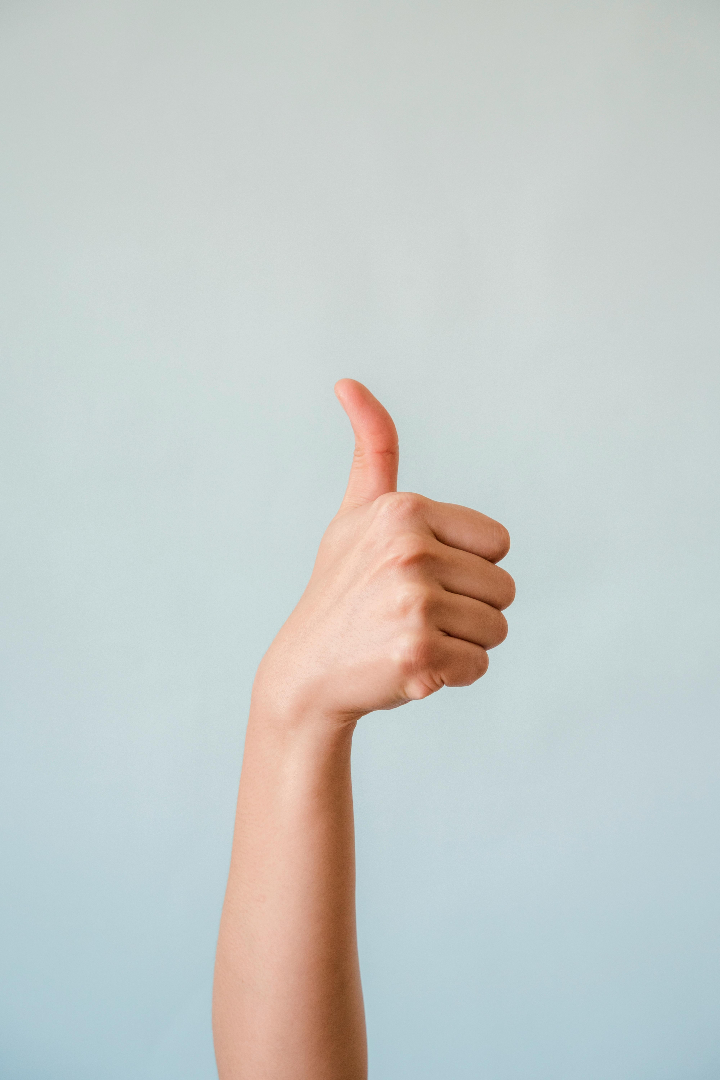 Close-up of a hand showing a thumbs up gesture on a blue background.