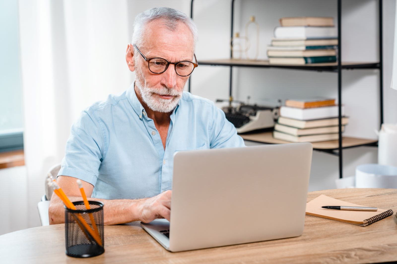 Older man sat at a desk looking at a laptop.