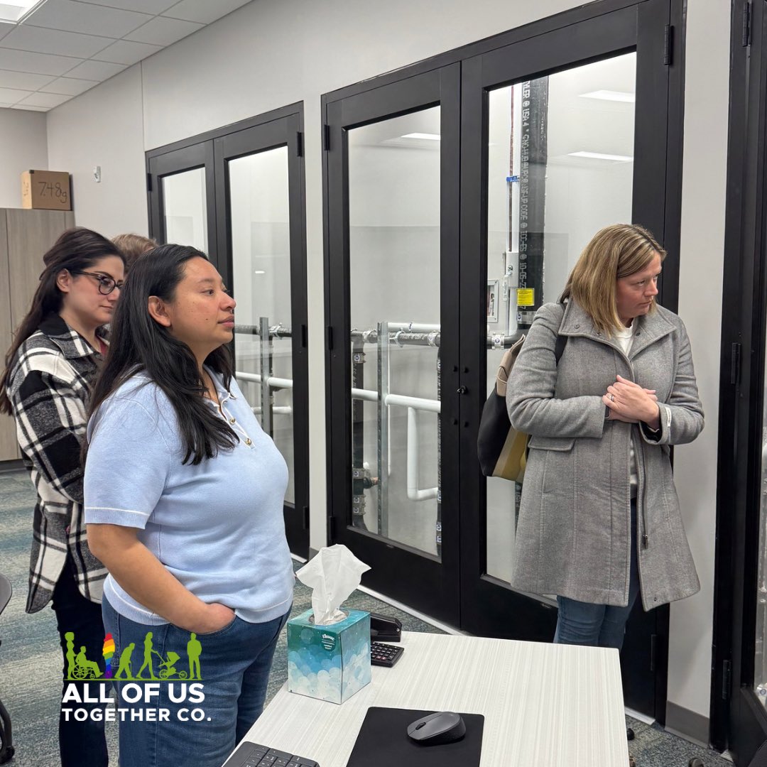 Three (3) diverse female professionals standing inside modern classroom. Company logo right in footer.