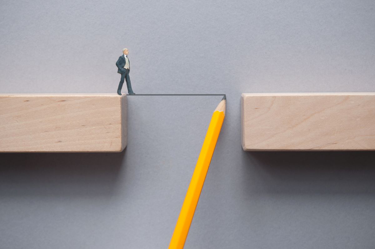 A miniature man standing at the edge of a wooden block gap. A pencil line is being drawn across the gap to the other side.