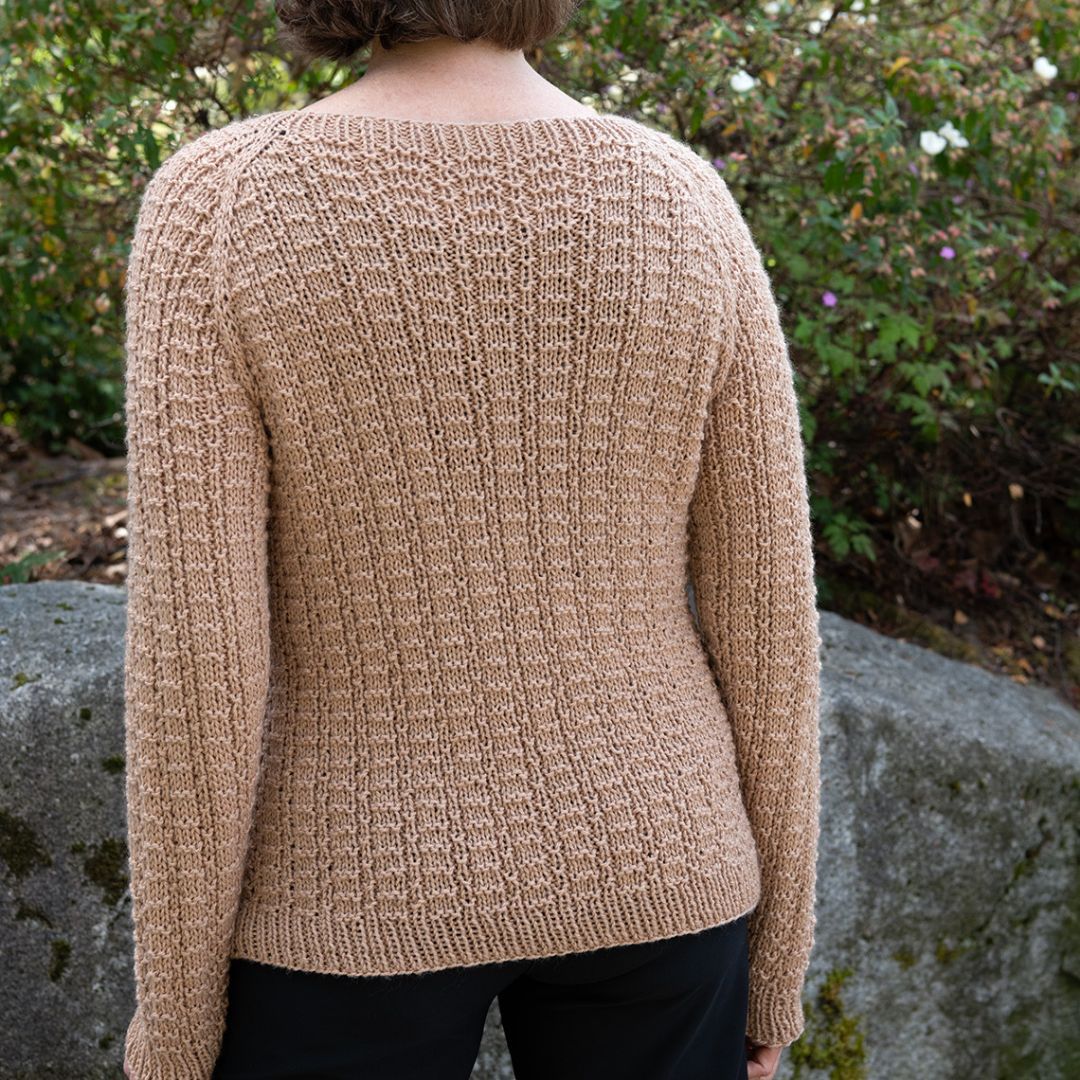 A backside view of a person is standing outside wearing the Fence Row Raglan Pullover, a Cascade Yarns free pattern, designed by Therese Chynoweth.