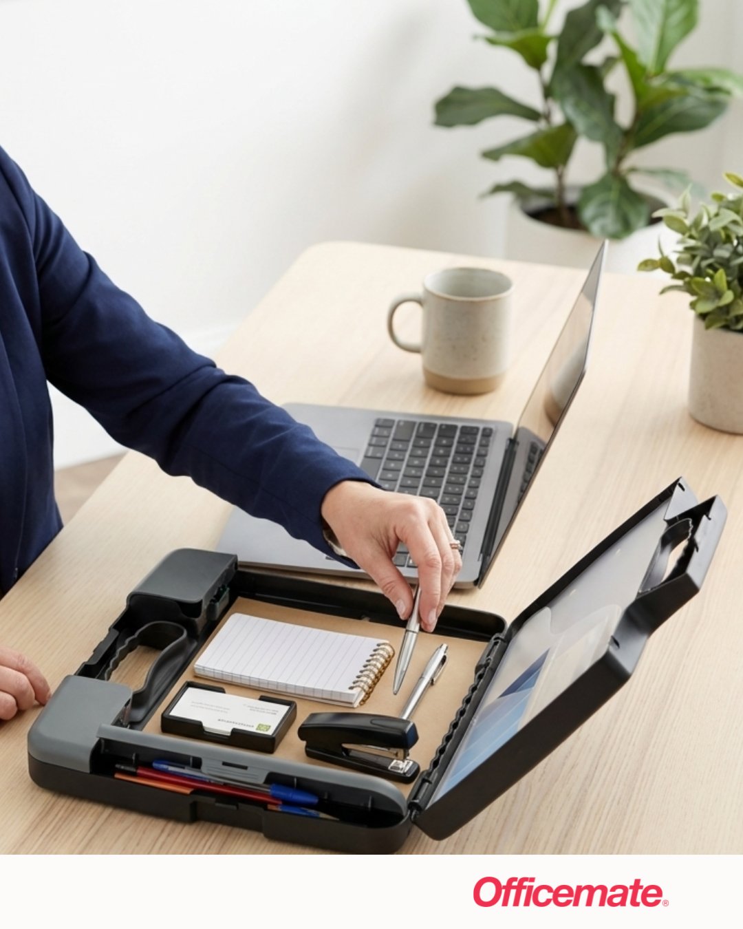 A person is organizing a portable office case on a desk. The case contains a notepad, pens, a stapler, and a USB flash drive. A laptop and a mug sit on the desk. A potted plant is in the background. The word "Officemate" appears at the bottom.