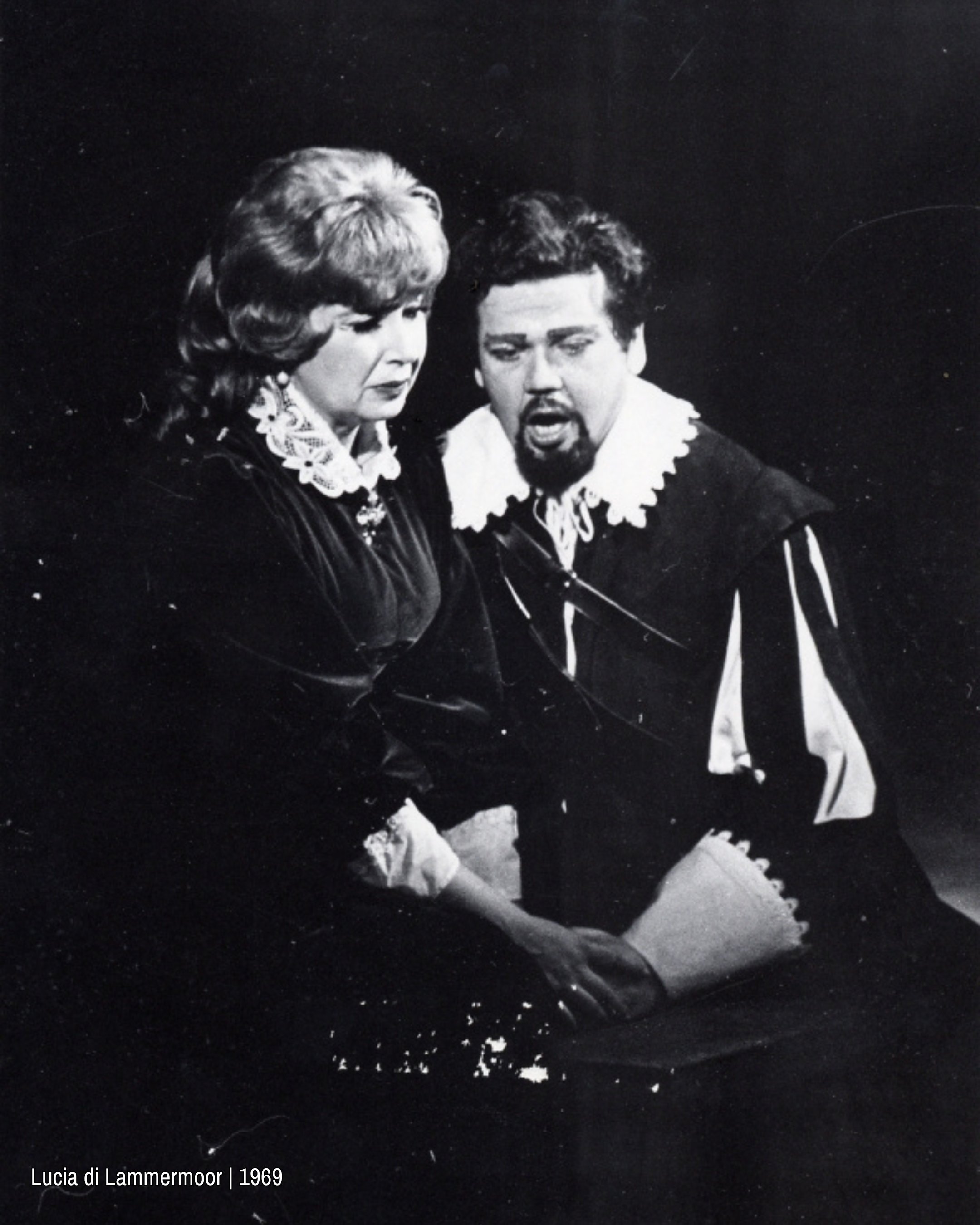 Black and white close-up of two singers in period costume, standing close together mid-performance, conveying tension and emotional intensity.
