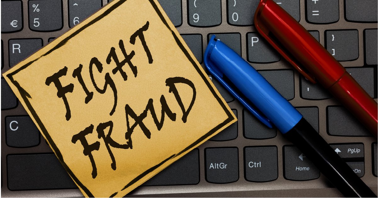 A sticky note with the words "Fight Fraud" is placed on a keyboard. Two pens, one red and one blue, are positioned beside the note.