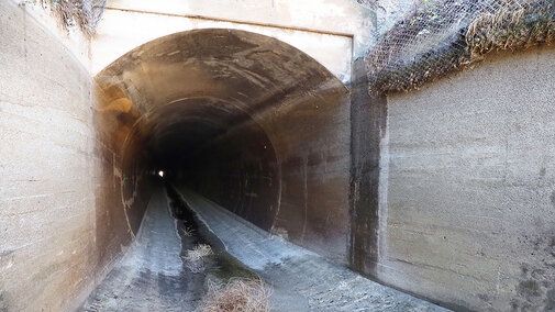 Closeup of empty canal tunnel entrance and tumbleweeds on ground