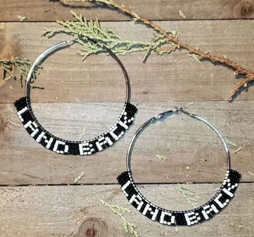 beaded silver tone hoop earrings with white beads that say LAND BACK on a background of black beads