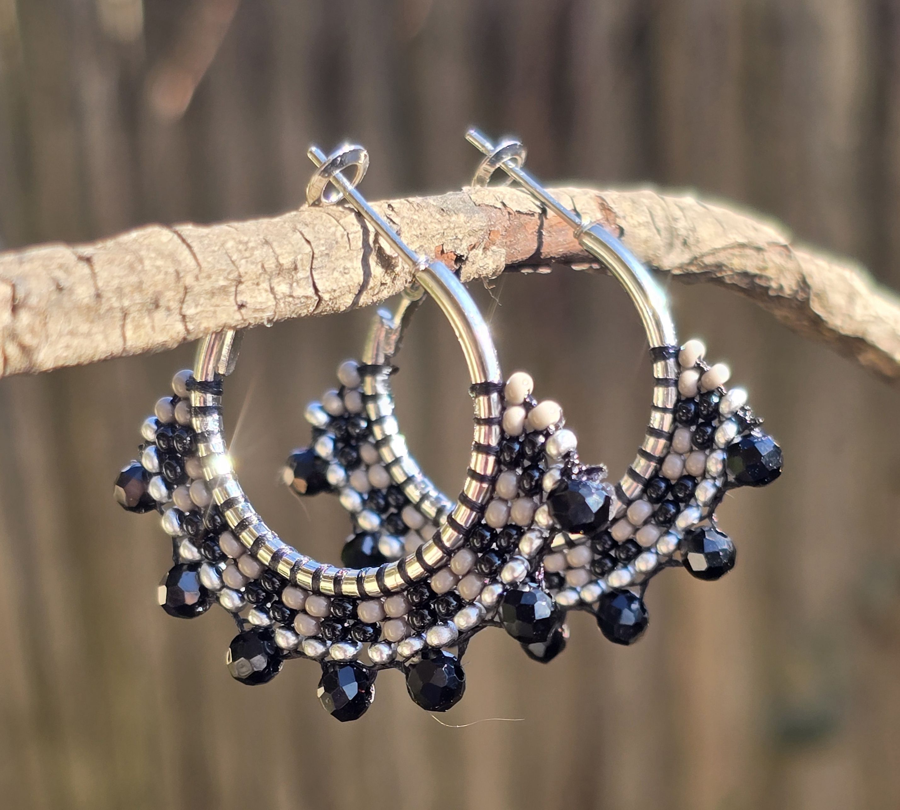silver-tone hoop earrings with beads in shades of black, gray, and silver, background of natural wood