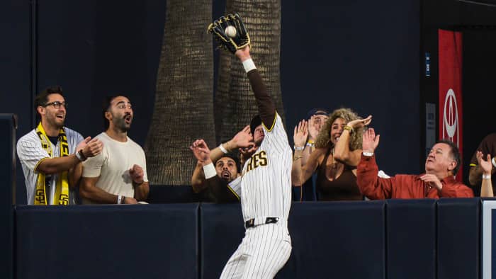 Jackson Merrill leaps to make a while wearing a white San Diego Padres uniform. Fans beyond the wall react.