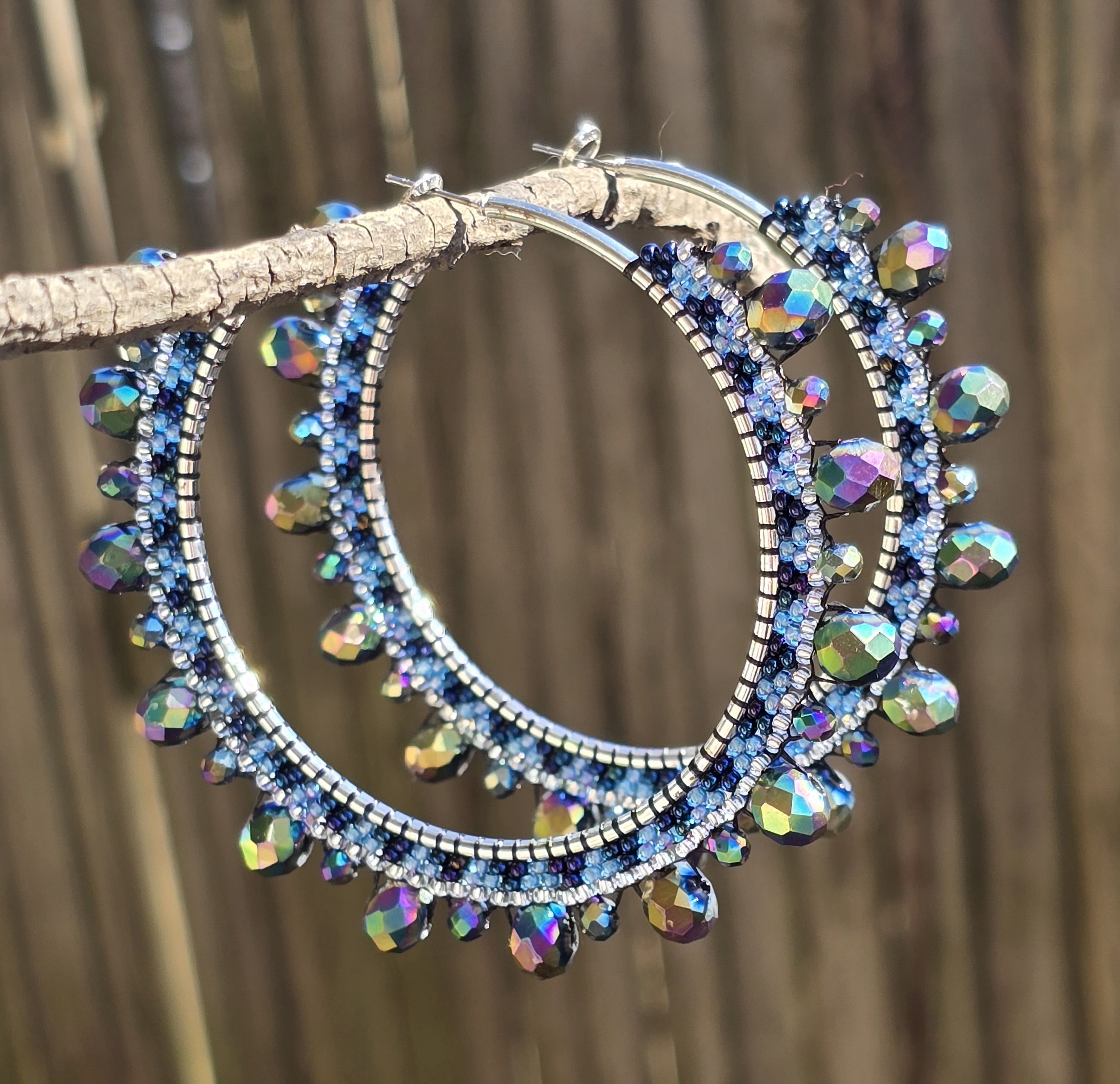silver tone hoop earrings with beads in shade if Iridescent blue, iridescent purple, and aurora borealis, background of natural wood