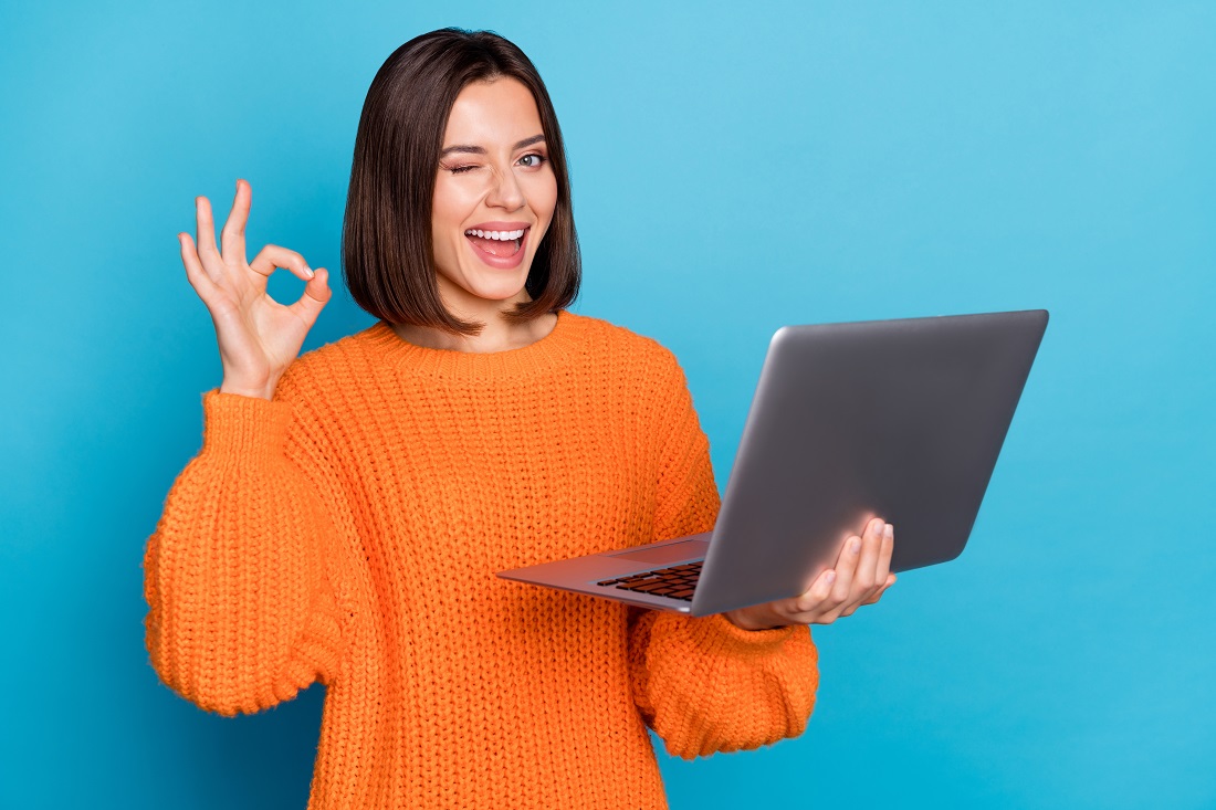 Smiling girl holding a laptop and giving an 'okay' sign.