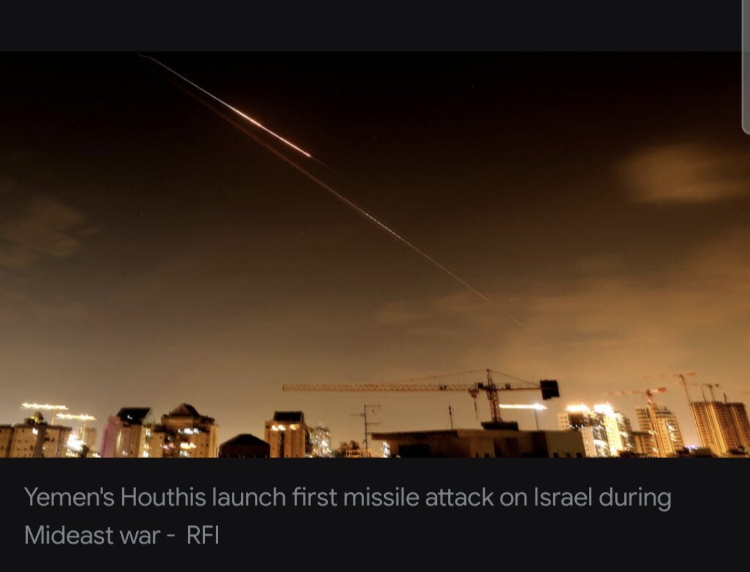 A dramatic nighttime shot of multiple bright missile trails streaking across a dark sky over a city skyline. Golden-white arcs of light cut through the blackness, like fireworks gone wrong, with Tel Aviv's high-rises glowing below—buildings lit up, smoke trails curling. Looks like Iron Dome intercepts lighting up the night, pure chaos in motion.