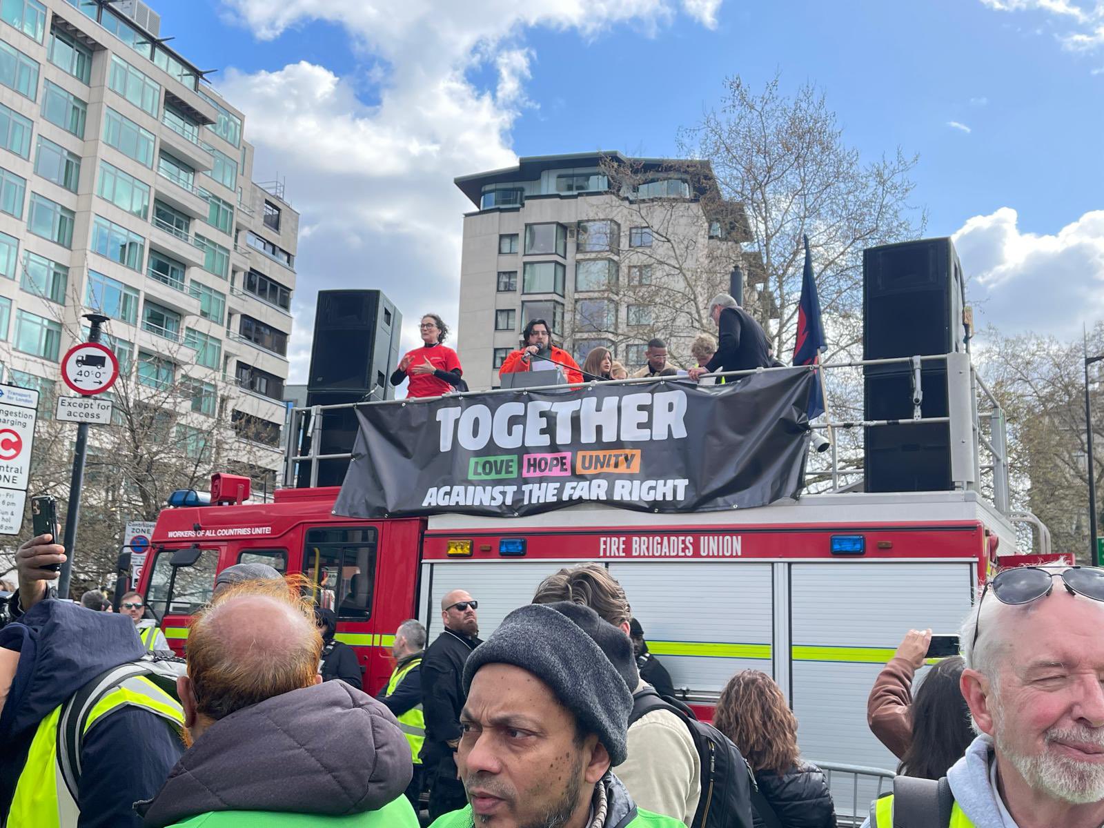 Image shows activists and BSL Interpreter standing on the campaign fire truck behind a black banner that says together against the far right
