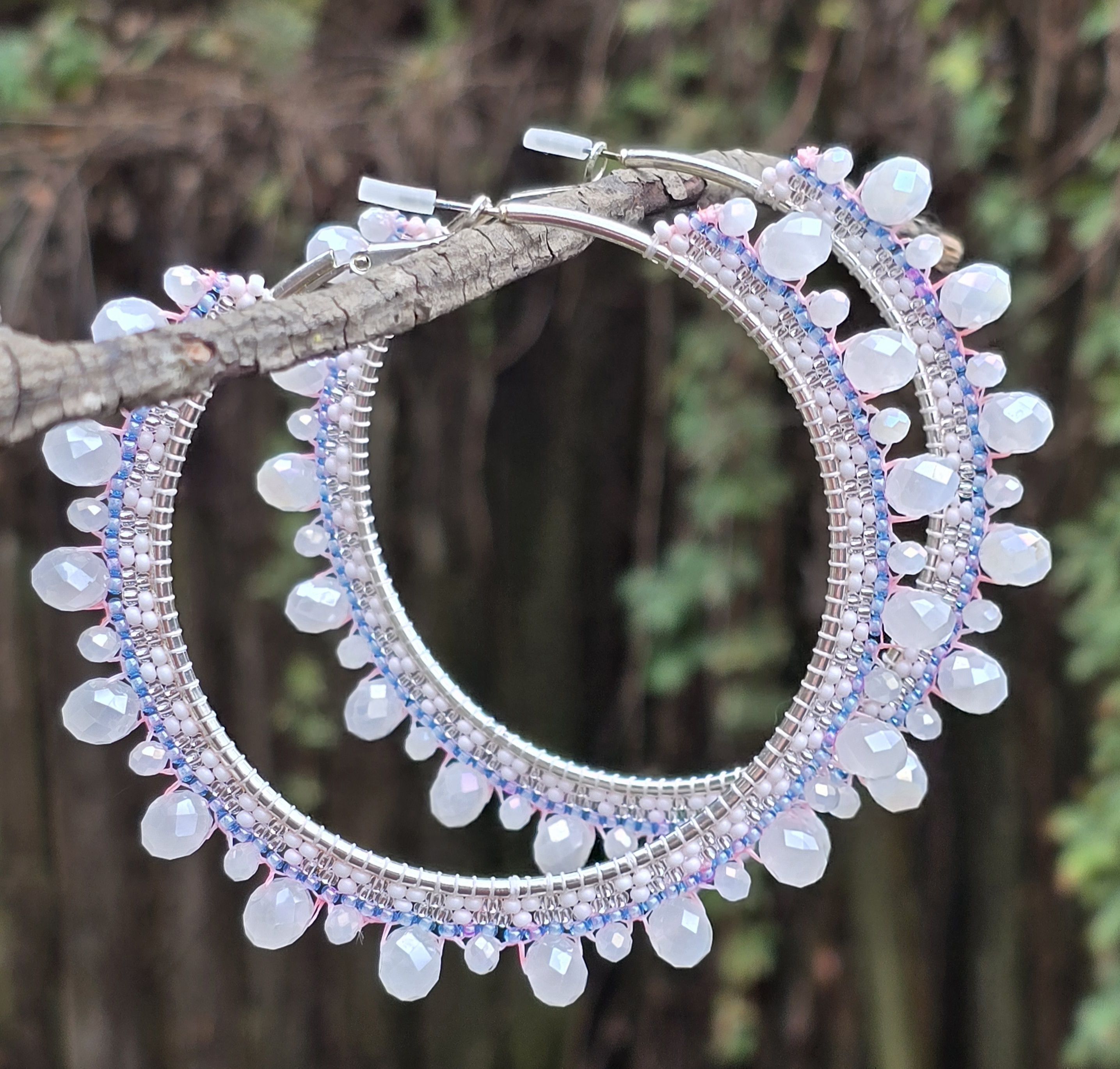 silver-tone beaded hoop earrings with glass beads in shades of white, silver, and purple/blue, natural green and wooded background