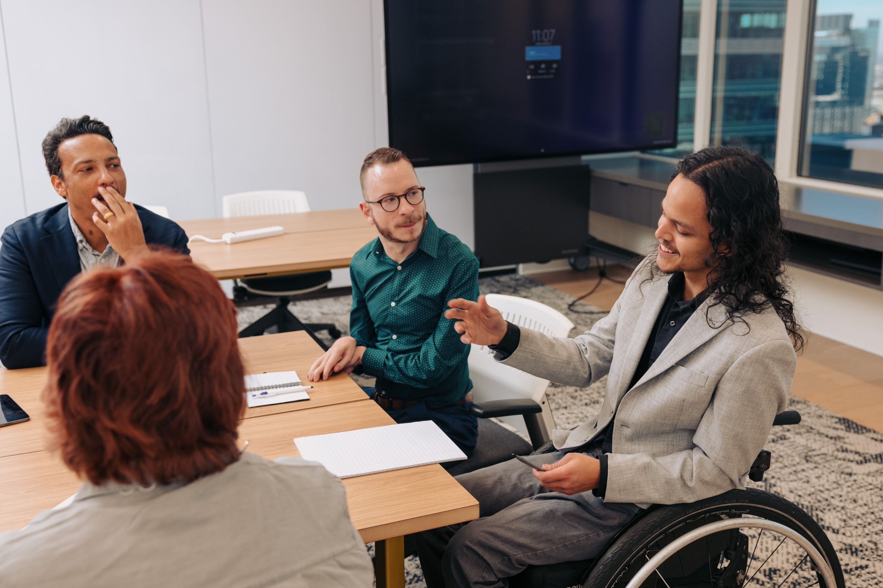 Jonathan Speaks in a Meeting
A young man who uses a wheelchair speaks to his colleagues during a meeting. They are seated around a conference table scattered with papers.

Photo Credit: Disability:IN