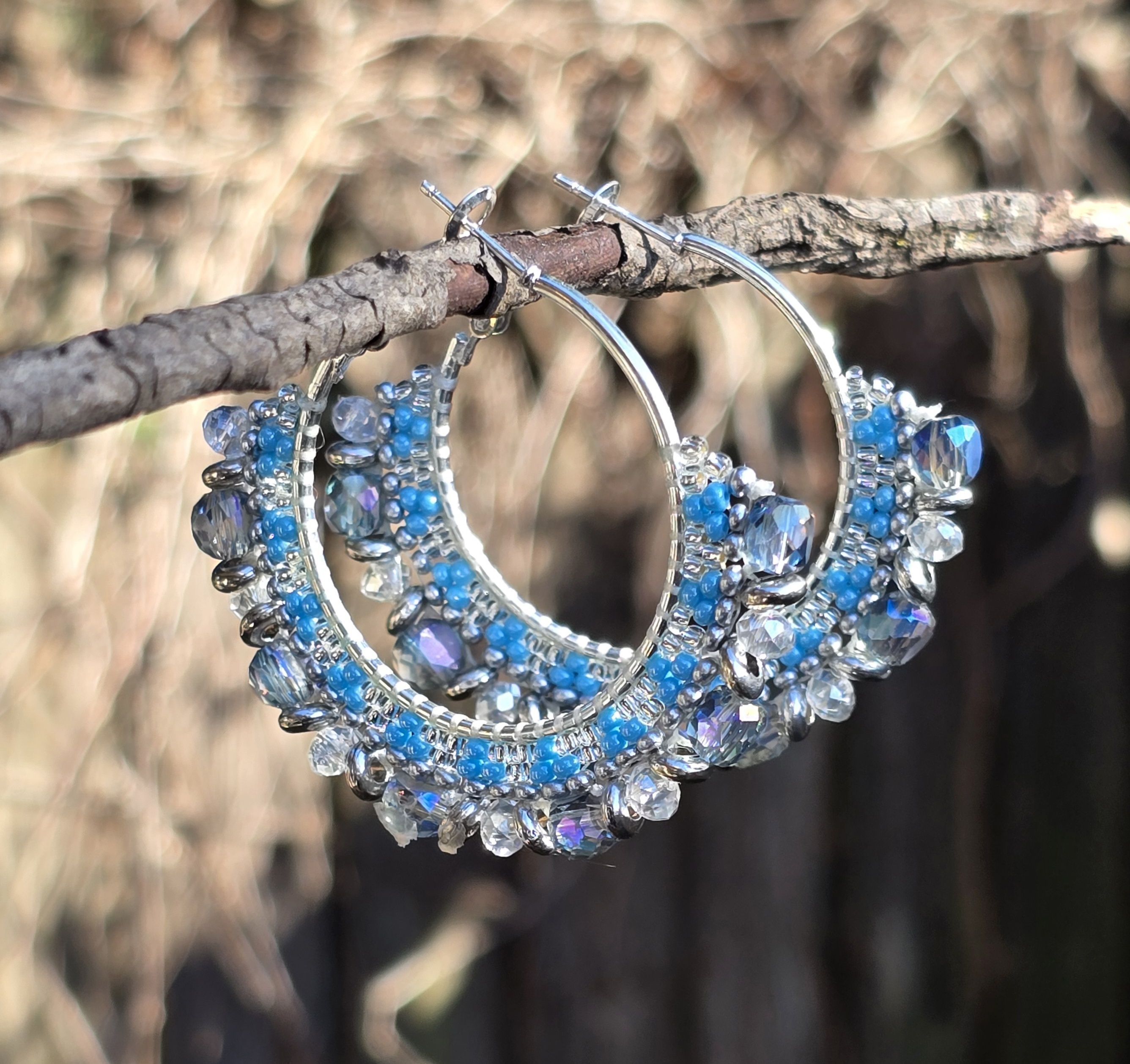 silver-plated hoop earrings with beads in shades of blue, clear, and silver, natural background of woods