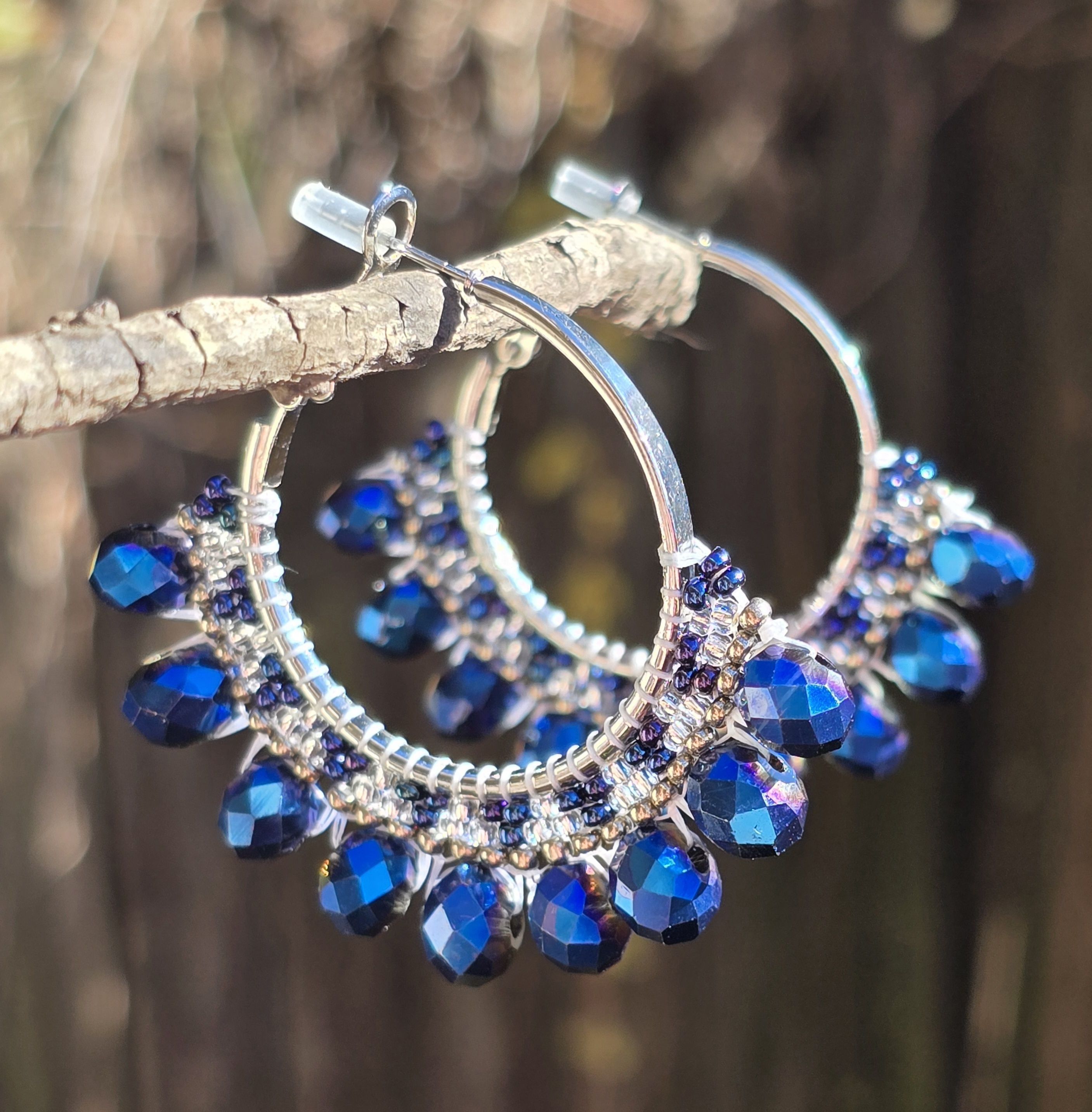 silver-tone hoop earrings with beads in shades of blue and silver, natural background of wood and leaves