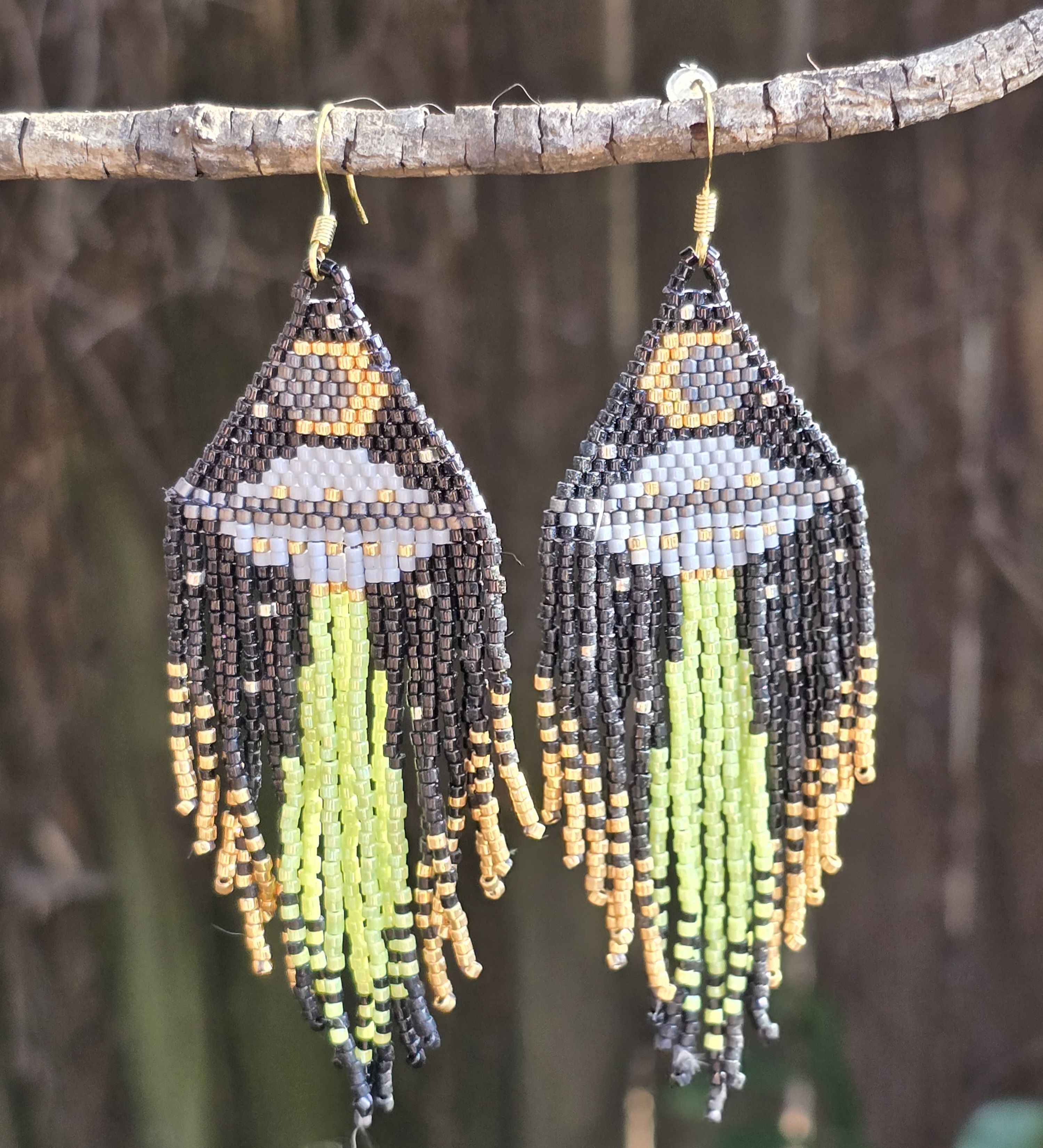 beaded earrings with black background, gray UFO, green light beam coming down, moon at top, gold specks for stars, background of natural wood
