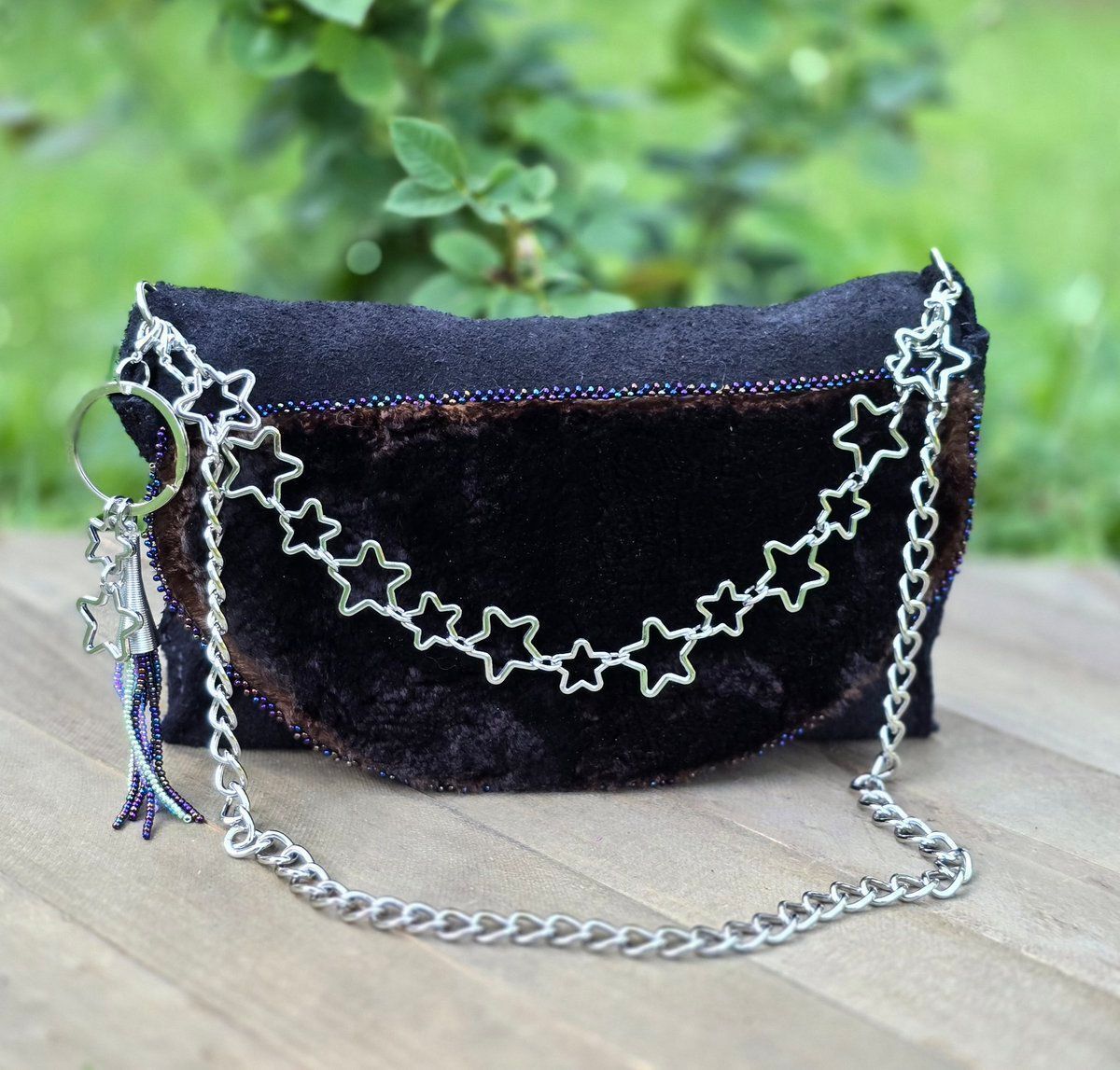 handbag made of black leather and natural seal skin, with glass aurora borealis shade beads, removable silver tone charms and chains, background of green grass and rose bush