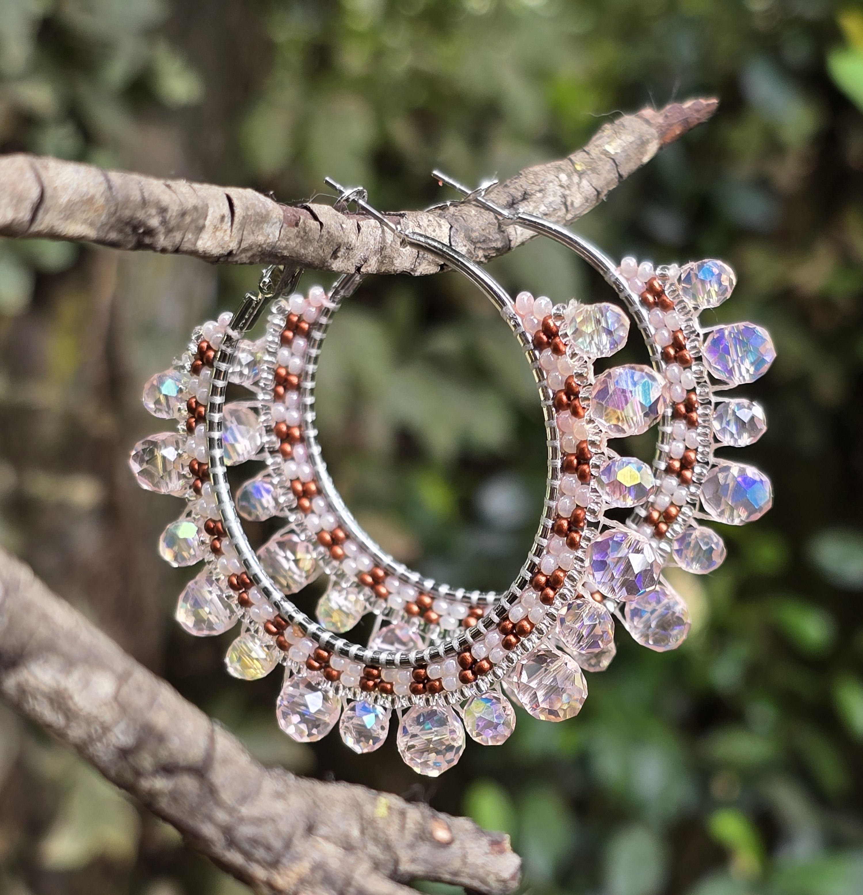 beaded silver tone hoop earrings with shades of brown, blush, and Iridescent, background of green leaves